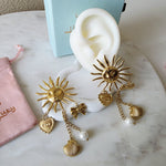 Gold sun-shaped earrings with pearl accents on a white ear model, placed on a marble surface.